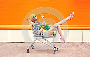 Fashion pretty cool girl in trolley cart having fun over colorful orange