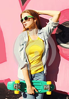 Fashion pretty cool girl wearing a sunglasses, jeans shirt and skateboard in city over colorful