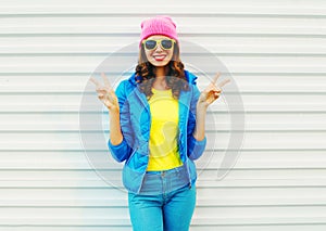 Fashion pretty cool smiling girl in colorful clothes having fun over white background wearing a pink hat yellow sunglasses