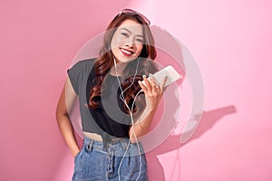 Fashion pretty cool smiling girl, relaxing, listening to music with headphones on a pink background