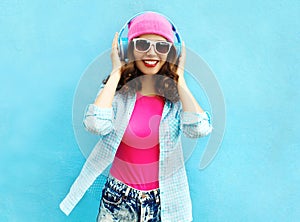 Fashion pretty cool smiling woman listens to music in headphones over colorful blue
