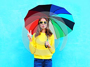 Fashion pretty cool woman holding colorful umbrella in autumn day over blue background wearing a yellow knitted sweater