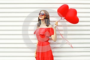 Fashion pretty happy smiling woman in red dress and sunglasses with air balloons heart shape looking up over white