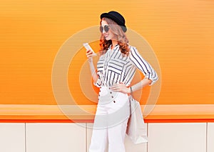 Fashion pretty happy young smiling woman model using smartphone with shopping bags wearing a black hat white pants over colorful