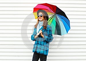 Fashion pretty smiling woman holds colorful umbrella wearing black hat checkered coat jacket over white