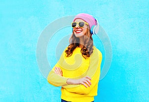 Fashion pretty smiling woman listens to music in headphones wearing a colorful pink hat, yellow sunglasses and sweater