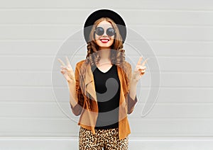 Fashion pretty smiling woman wearing a black hat, sunglasses and jacket over urban background