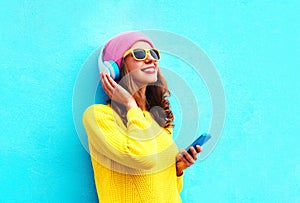 Fashion pretty sweet carefree girl listening to music in headphones with smartphone wearing a colorful pink hat yellow sunglasses