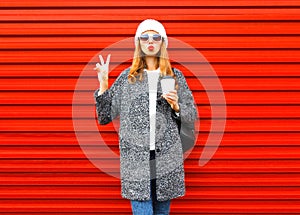 Fashion pretty woman with coffee cup in coat posing on red