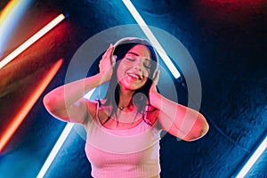 Fashion pretty woman with headphones listening to music over neon background at studio.