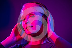 Fashion pretty woman with headphones listening to music over red neon background at studio