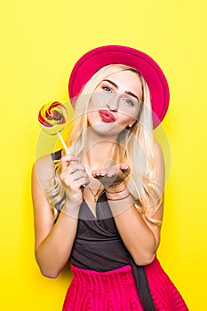 Fashion pretty woman sends air sweet kiss with candy wearing a red hat and yellow color clothes over colorful yellow background