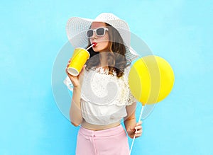 Fashion pretty woman in straw hat with air balloon drinks fruit juice from cup over colorful blue
