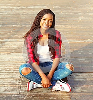 Fashion pretty young african woman sitting in the city park, wearing a red checkered shirt