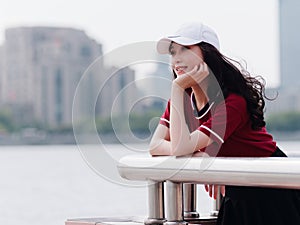 Fashion pretty young girl with black long hair, wearing red T-shirt and white baseball cap posing outdoor, minimalist urban clothi
