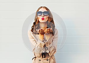 Fashion pretty young woman blowing red lips sends sweet kiss wearing a black sunglasses coat over grey
