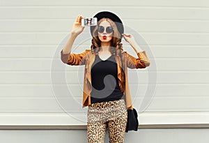 Fashion pretty young woman model taking photo picture self-portrait on smartphone wearing retro elegant hat, sunglasses