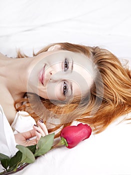 Fashion red-haired girl with rose in the bedroom.