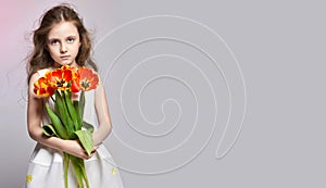 Fashion red-haired girl with tulips in hands. Studio photo on light coloured background. Birthday, holiday, mothers day, first day