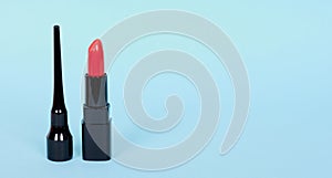 Fashion red lip stick with black mascara tube, make up. Isolated on blue background, copy space