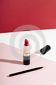 Fashion red lipstick and pencil top view composition. Beauty industry product concept. Glamorous makeup accessory close up on pink photo