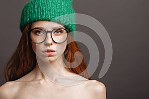 Fashion redhead Girl in Knitted Hat and galsses on grey background