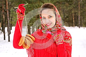 Fashion in Russian style. A beautiful girl in a red Pavlovsky Posad shawl holds bagels in the hands of a winter forest