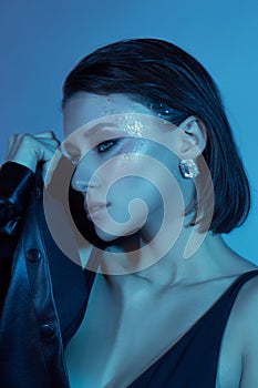 Fashion sexy young woman neon light posing in the studio. Beauty makeup portrait of a woman blue light. Slim body, black leather