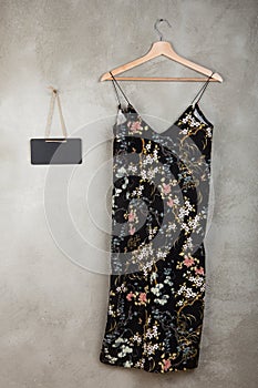 Fashion and shopping concept - blank blackboard and beautiful little black dress in floral pattern on a hanger