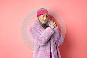 Fashion and shopping concept. Cool and stylish asian old woman in winter coat making finger gun gesture and looking
