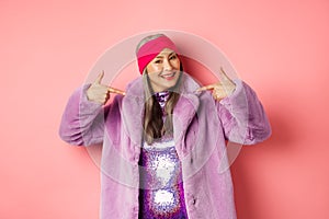 Fashion and shopping concept. Cool and trendy asian senior woman pointing fingers at herself, dressed in stylish purple