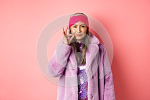 Fashion and shopping concept. Cunning asian senior woman in stylish clothes keeping secret, squinting and looking