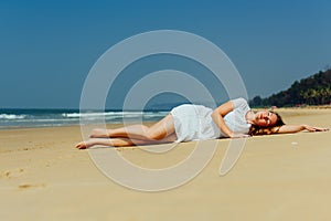 Fashion shot of a beautiful girl in a white dress lying on the beach. Goa India