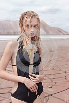 Fashion shot of beautiful blonde girl black bathing suit with a bright make-up on a background of mountains in pustyle