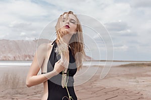 Fashion shot of beautiful blonde girl black bathing suit with a bright make-up on a background of mountains in pustyle