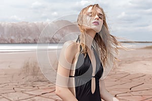 Fashion shot of beautiful blonde girl black bathing suit with a bright make-up on a background of mountains in pustyle