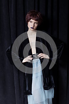 Fashion shot of a beautiful young girl with a cheeky short hair style hipster in black velvet jacket in a studio on a black backgr