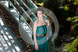 Fashion slim woman wearing green dress standing against bridge