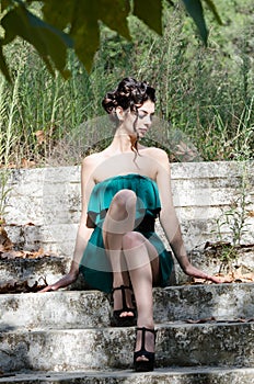 Fashion slim woman wearing green strapless short dress sitting on old and dirty cement stairs