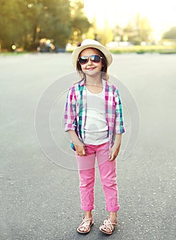 Fashion smiling little girl child wearing a checkered pink shirt, hat and sunglasses