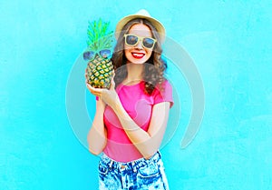 Fashion smiling woman with pineapple sunglasses wearing summer hat having fun over colorful blue