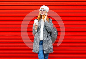 Fashion smiling woman talks on a smartphone holds coffee cup on a red