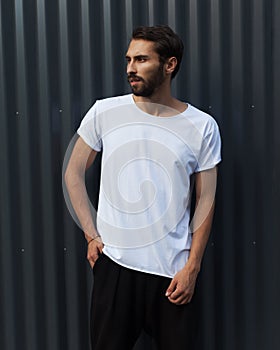Fashion street youth. A man in a white T-shirt posing on a dark blue metallic background in the summer evening. Cover.