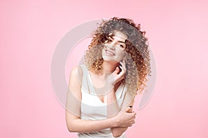 Fashion studio portrait of beautiful smiling woman with afro curls hairstyle isolated over pink background . Fashion and