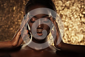 Fashion studio portrait of an extraordinary beautiful african american model with closed eyes over golden background