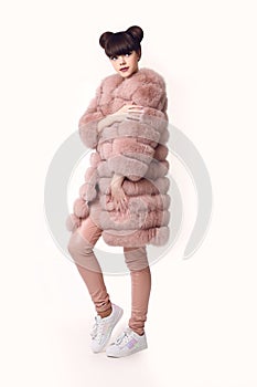 Fashion studio teen look style in pink fur coat and sneakers shoes. Fashionable young girl with ears hairstyle wears leather pant