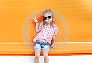 Fashion stylish little girl child wearing sunglasses and checkered shirt having fun in city