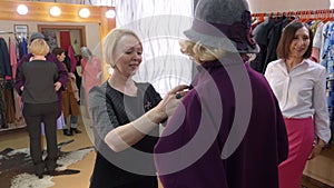 Fashion stylist helping to choose new coat for mature woman in clothes boutique. Senior woman trying coat in fashion