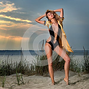 Fashion summer lifestyle photo of young woman with tanned perfect body wearing black swimsuit and shirt on the beach.
