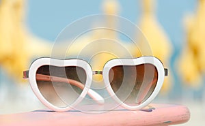 Fashion sunglasses heart shaped on beach background with yellow parasols